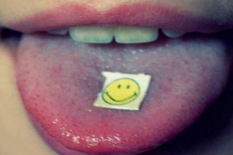 Close-up of a person holding a blotter with a smiley face on their tongue, symbolizing the use of legal LSD analogs like 1P-LSD, 1D-LSD, 1V-LSD, and 1S-LSD.