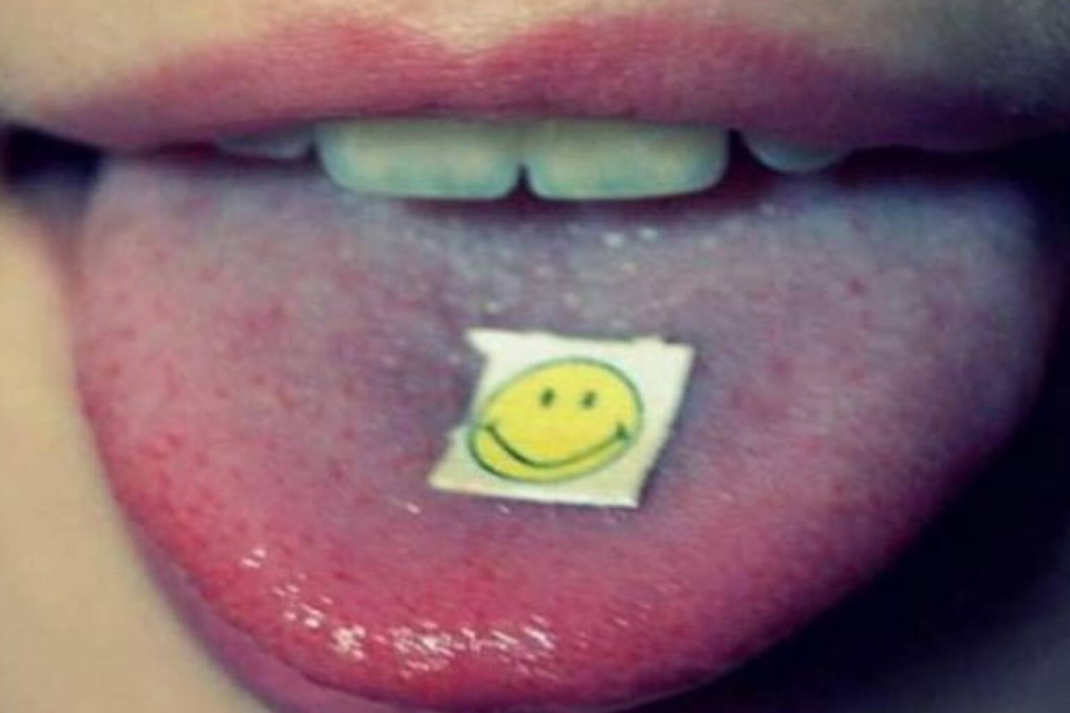 Close-up of a person holding a blotter with a smiley face on their tongue, symbolizing the use of legal LSD analogs like 1P-LSD, 1D-LSD, 1V-LSD, and 1S-LSD.